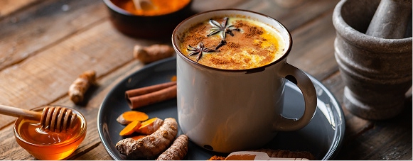 Turmeric hot chocolate topped with cacao nibs beside turmeric root and powder